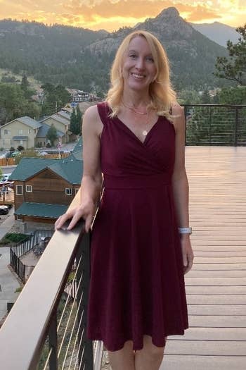 a reviewer in a v-neck burgundy dress standing on a balcony with a mountain landscape in the background