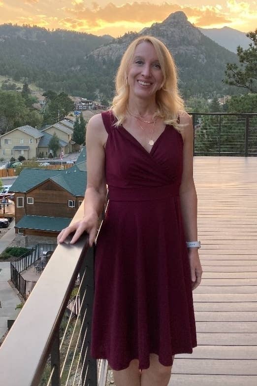a reviewer in a v-neck burgundy dress standing on a balcony with a mountain landscape in the background