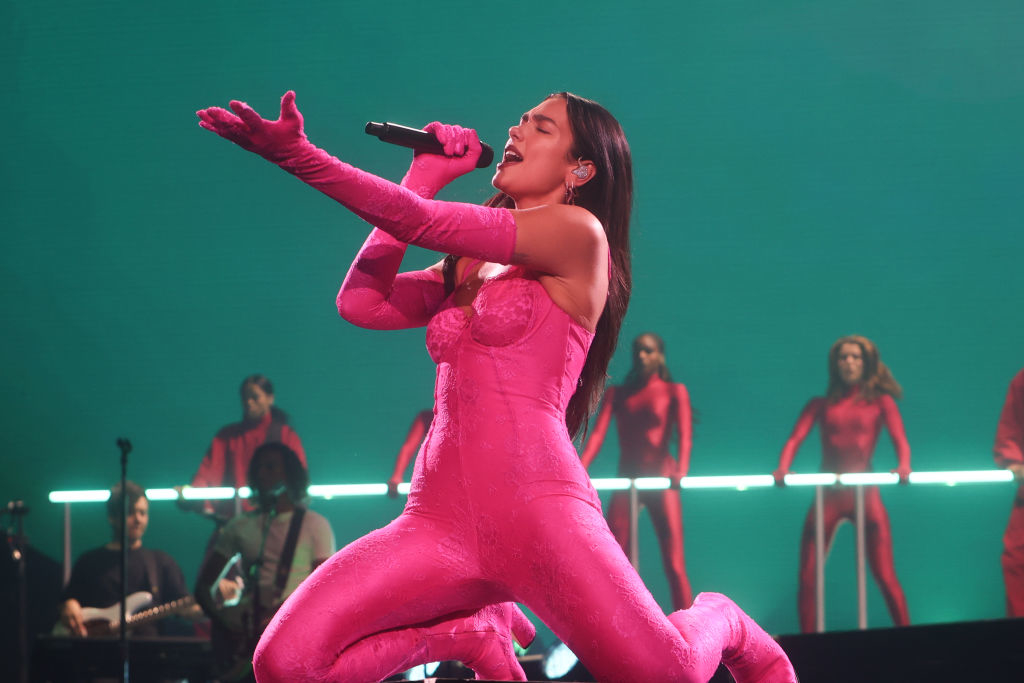 Dua Lipa performing on stage with backup singers and musicians in the background