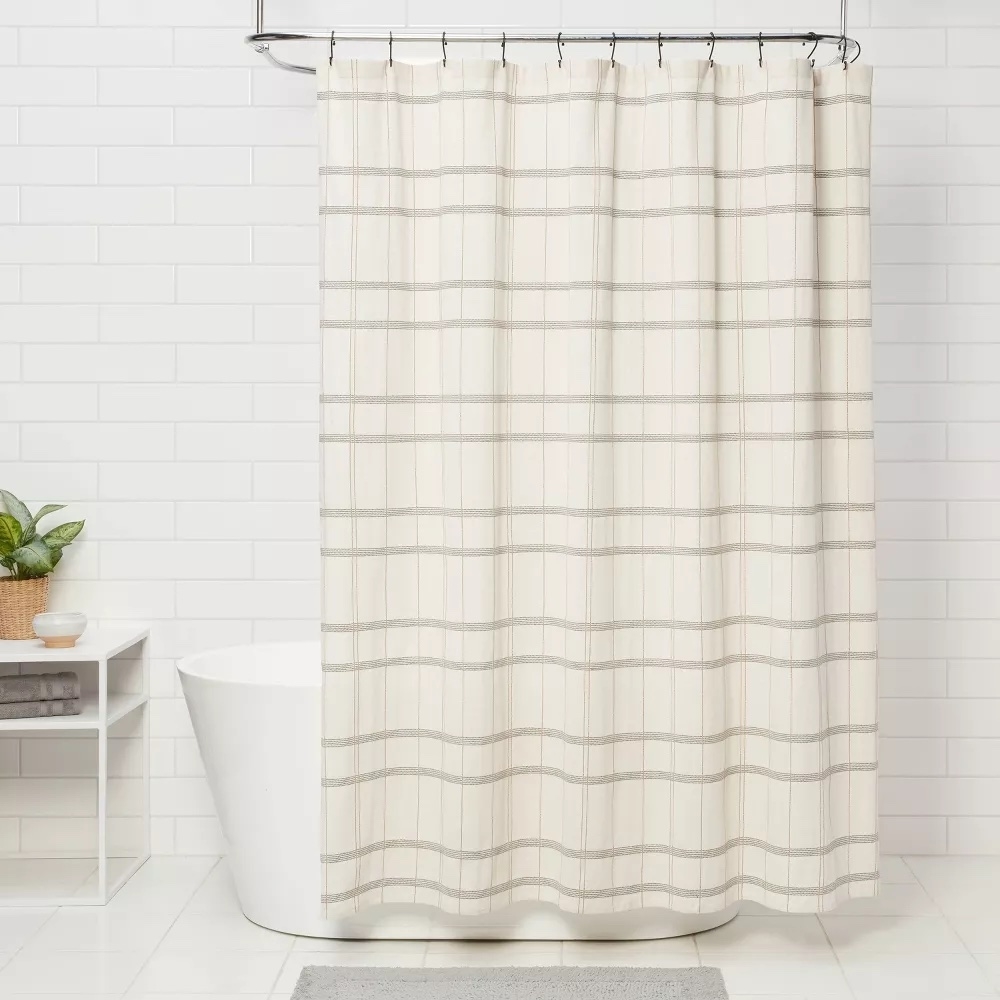 Beige shower curtain with horizontal stripes, hanging in a white-tiled bathroom