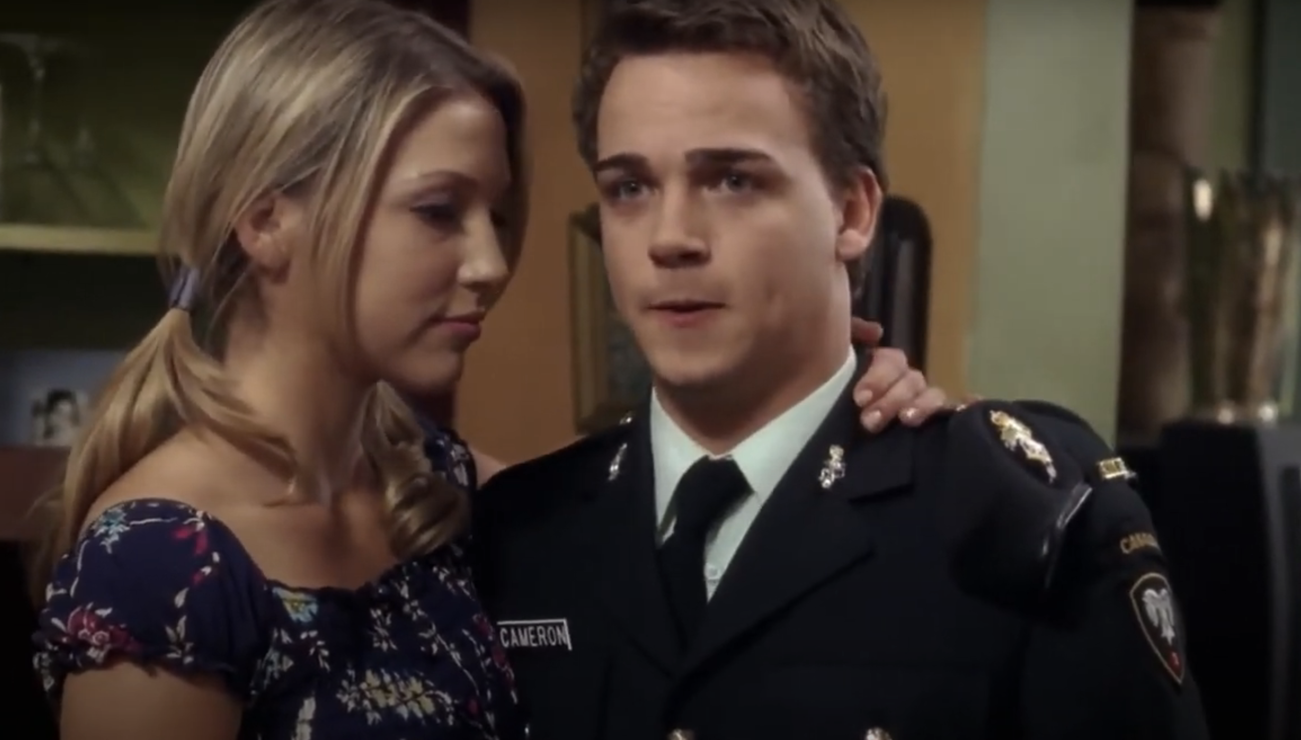 Two characters from a TV show embrace, the man in a dress uniform with &quot;CAMERON&quot; tag, and the woman in a floral dress