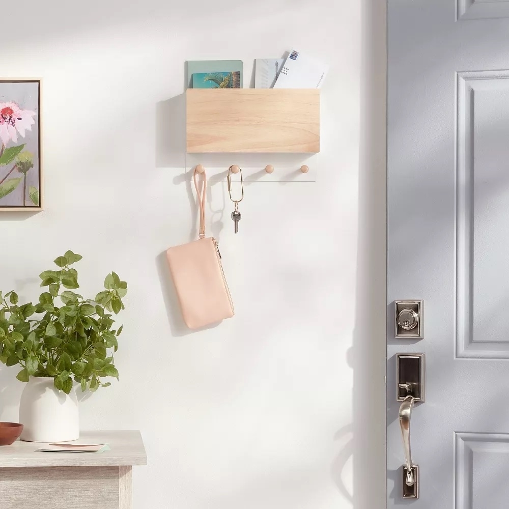 Wall-mounted shelf with keys, small plant on side table, and hanging pink purse near an open door