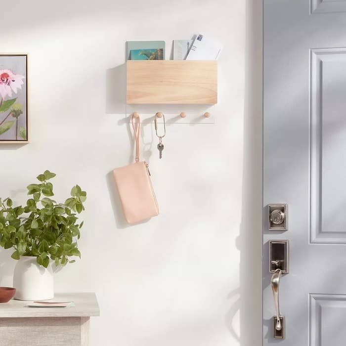 Wall-mounted support  with keys, tiny  works  connected  broadside  table, and hanging pinkish  purse adjacent   an unfastened  door
