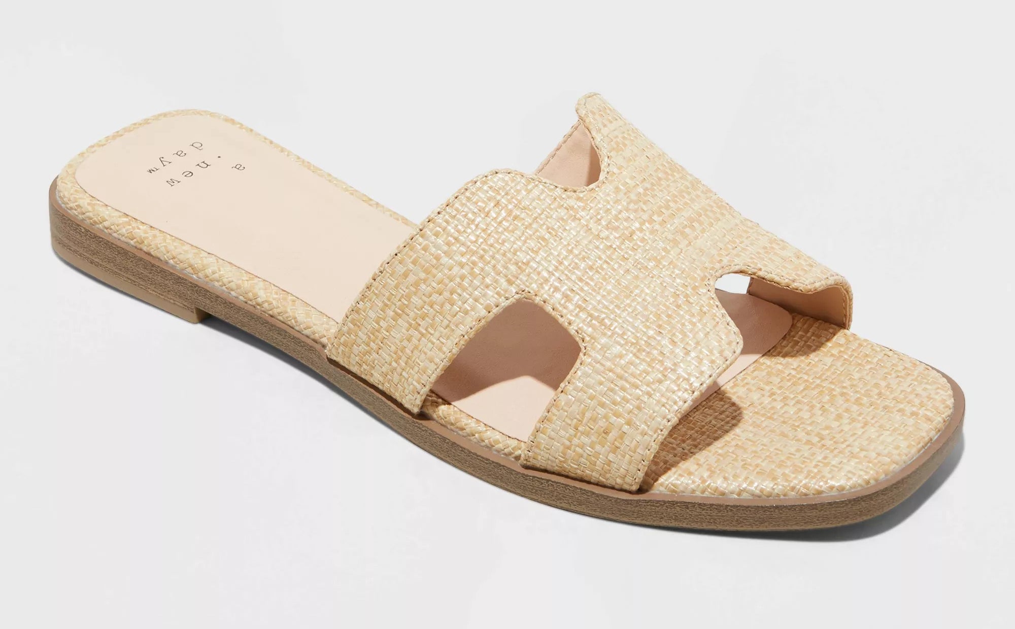 Flat slip-on sandal with textured raffia-like material, open toe, and single strap across the foot