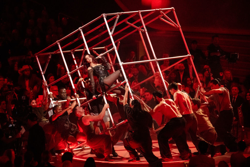 Performer in a cage-like structure with attendants around at a high-profile event