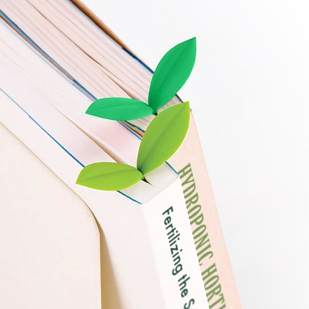 A green sprout-shaped bookmark nestled between the pages of a book