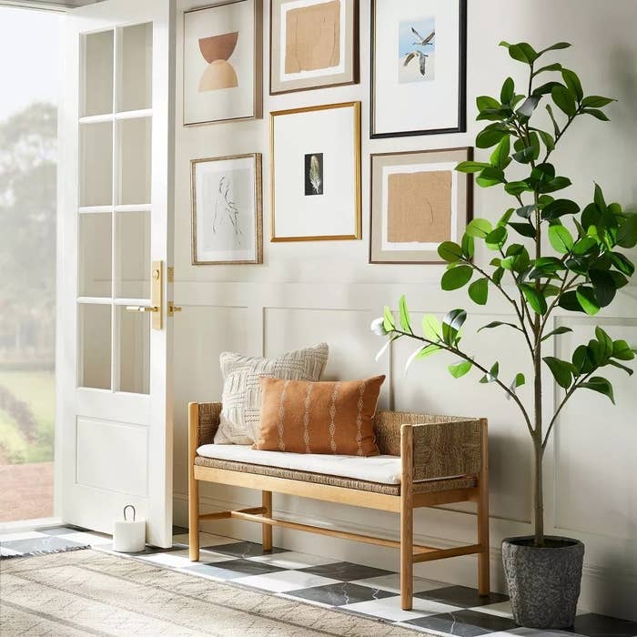 Entryway bench with pillows next to a potted plant and gallery wall