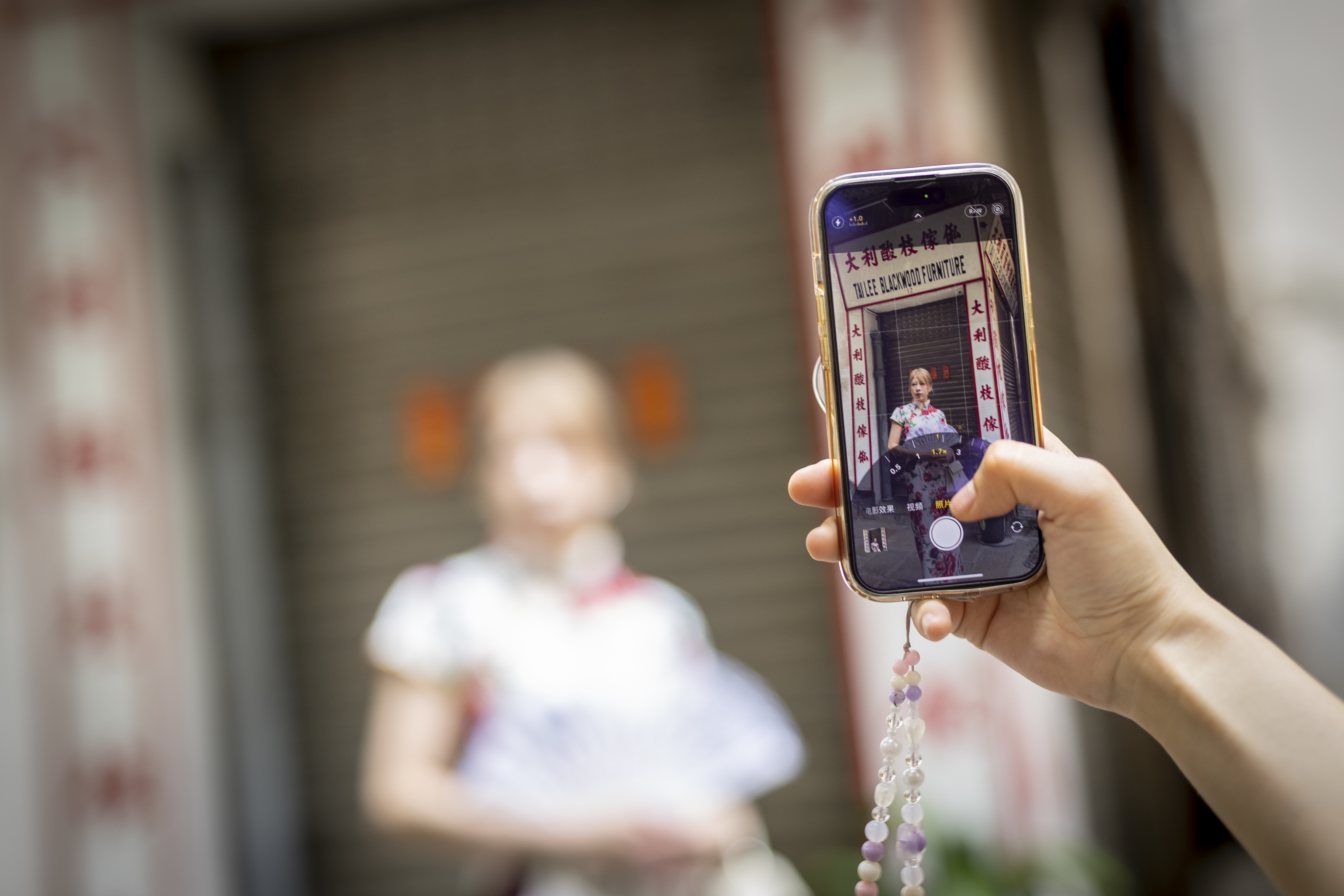 Person holds smartphone capturing another person posing, both out of focus, screen in focus displaying camera interface