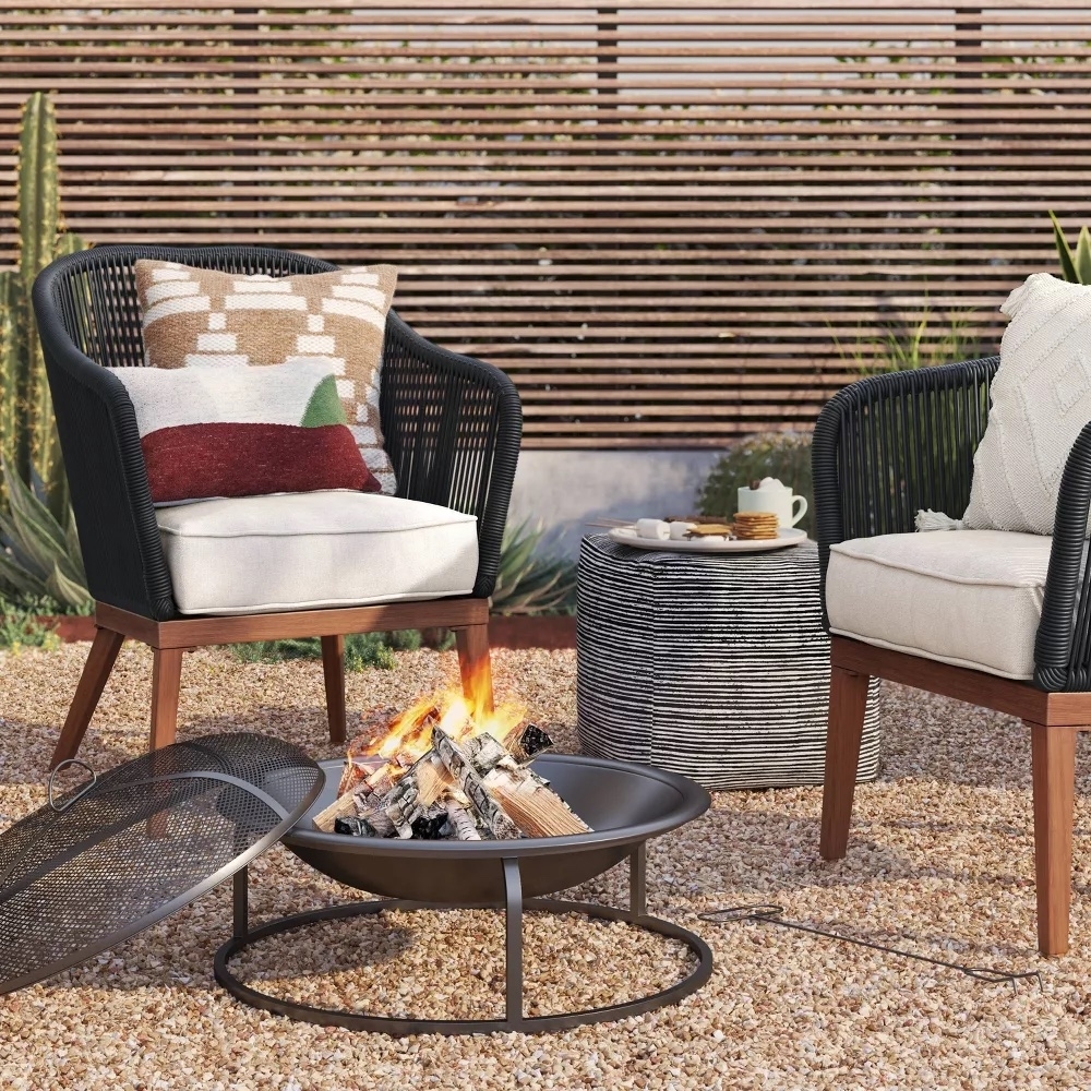 Two patio chairs with cushions by a fire pit, with a side table and outdoor pillows, suggesting cozy outdoor furnishing options