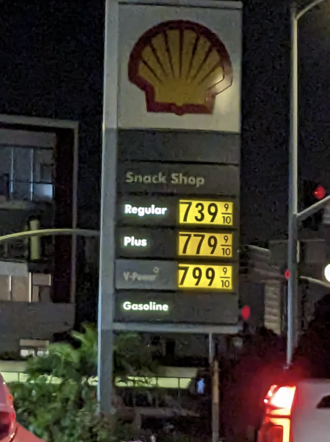 Gas station sign with high fuel prices, snack shop advertisement above