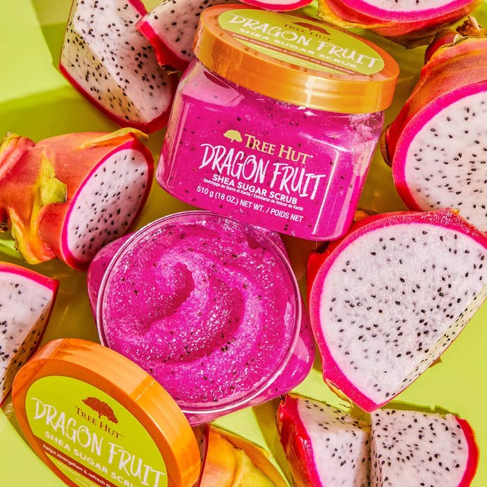 The open container, showing the hot pink scrub&#x27;s texture, surrounded by dragon fruit slices on a yellow background
