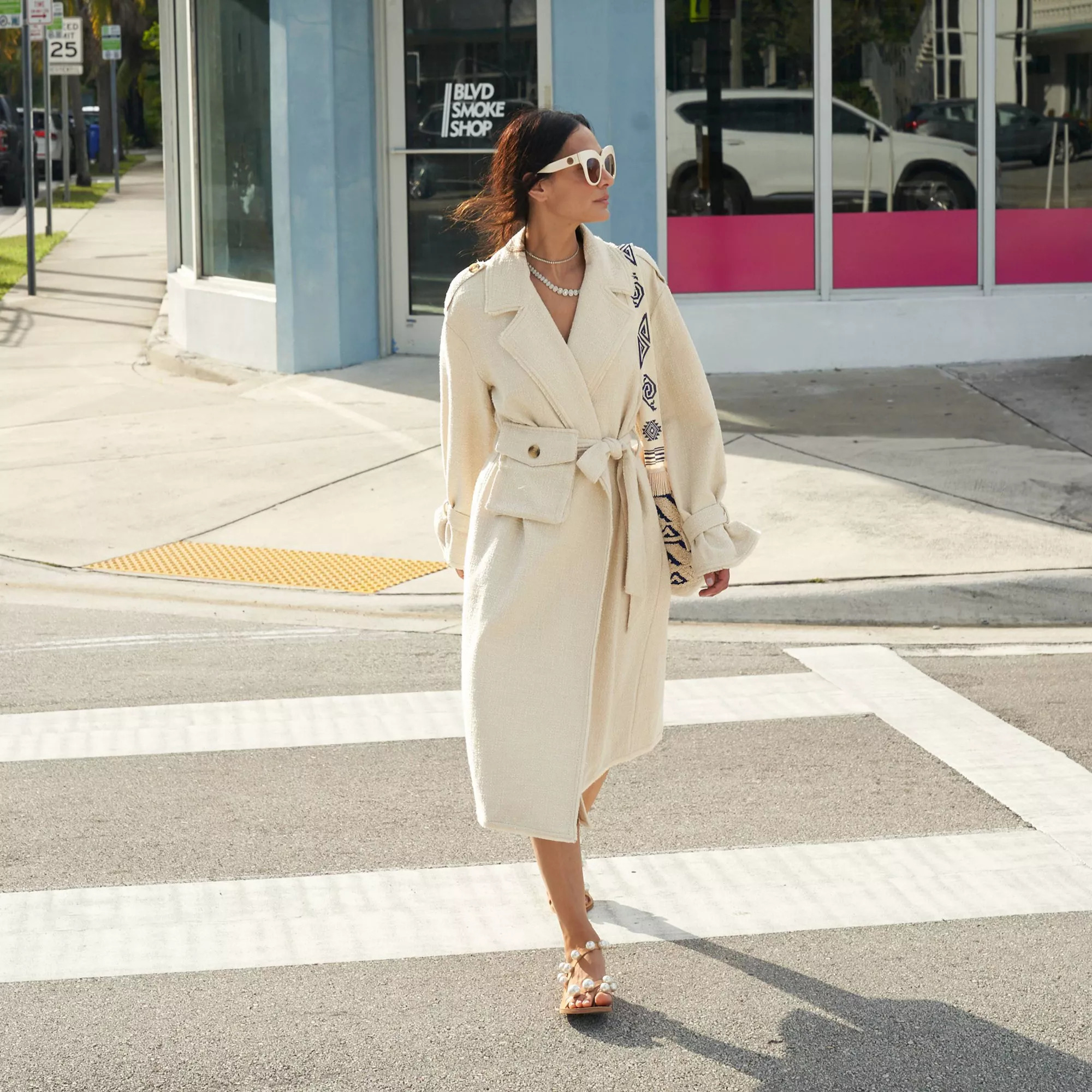Model wearing the below knee-length beige trench coat in a mid-weight boucle fabric, dropped shoulders, and tie-waist