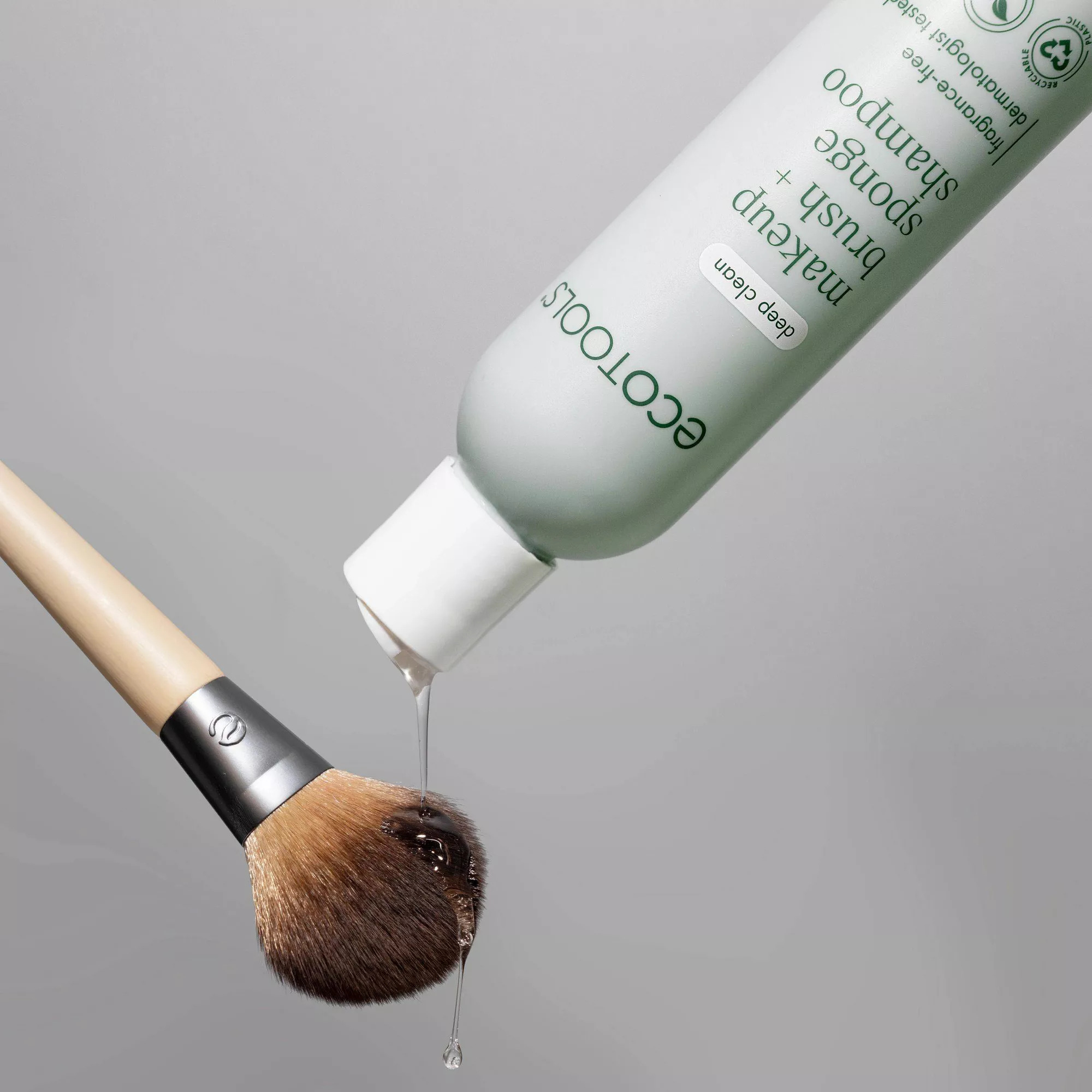 A bottle of Ecotools makeup brush shampoo with a small amount dripping onto a makeup brush