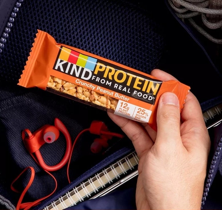 Hand reaching for a KIND Protein bar in a bag with headphones and keys