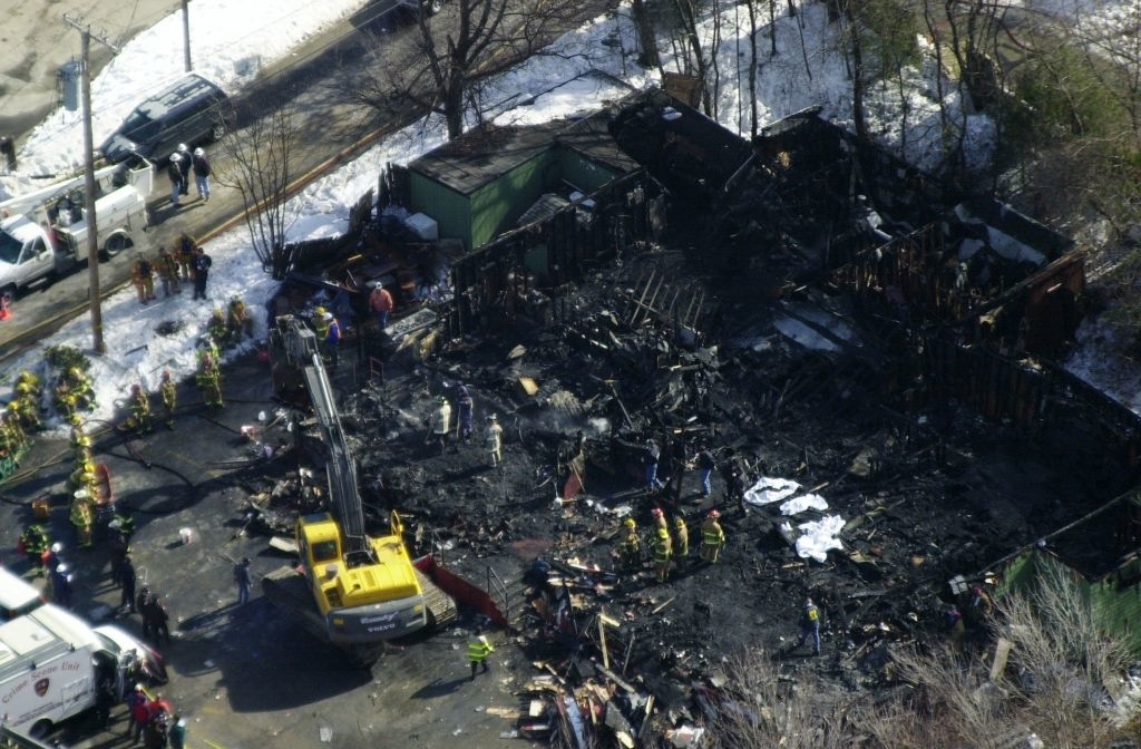 Aerial view of a burned-down structure with firefighters and a crane amidst debris