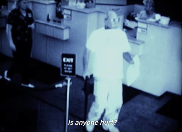 Black and white security footage showing someone at a counter with text &quot;Is anyone hurt?&quot;