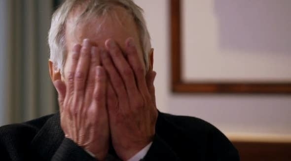 Robert Durst with hands covering his face in a gesture of despair or fatigue