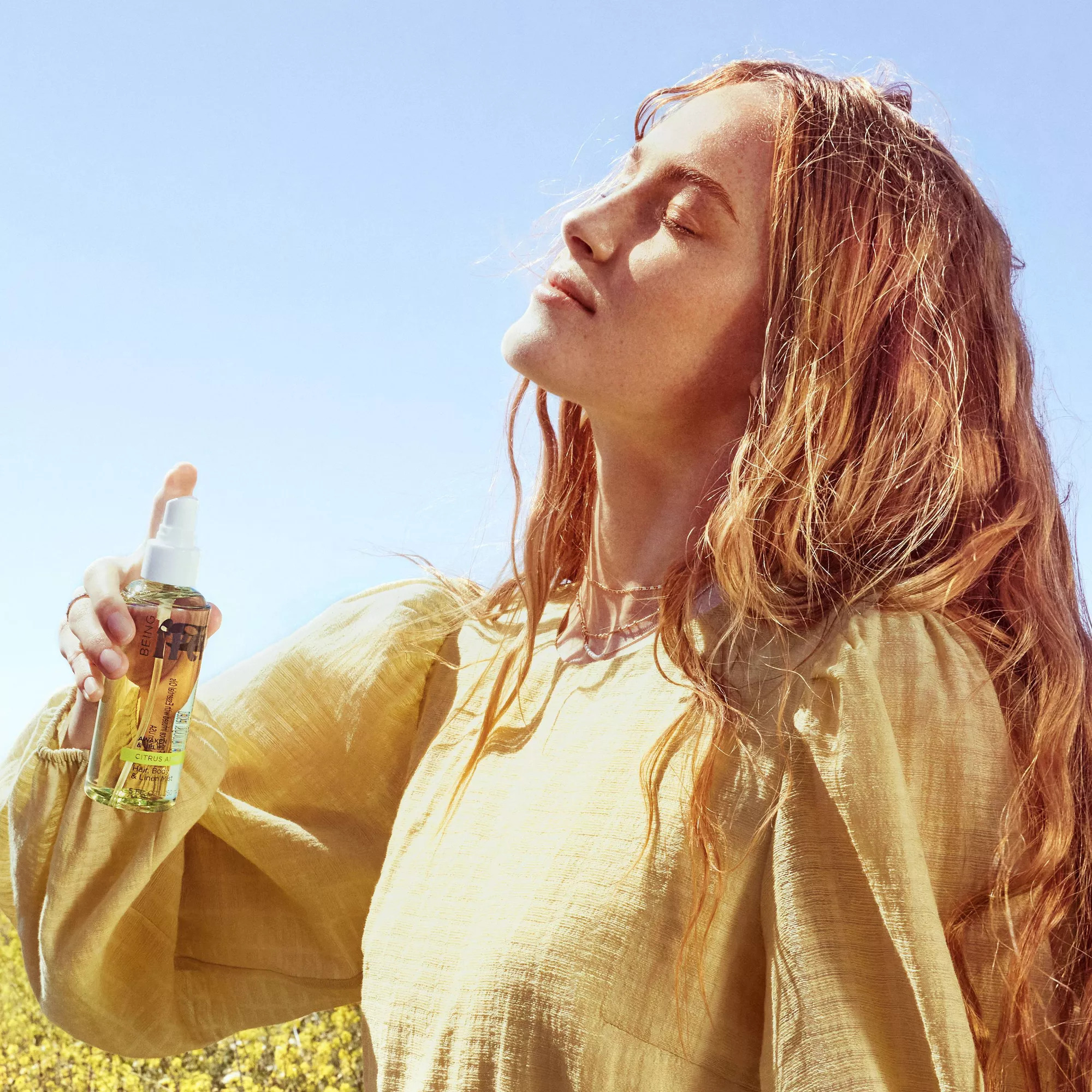 Person holding the spray bottle, eyes closed, in a relaxed pose with a sunny backdrop