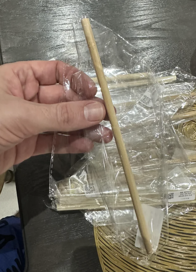 Hand holding a single chopstick above several pairs of chopsticks in plastic wrapping