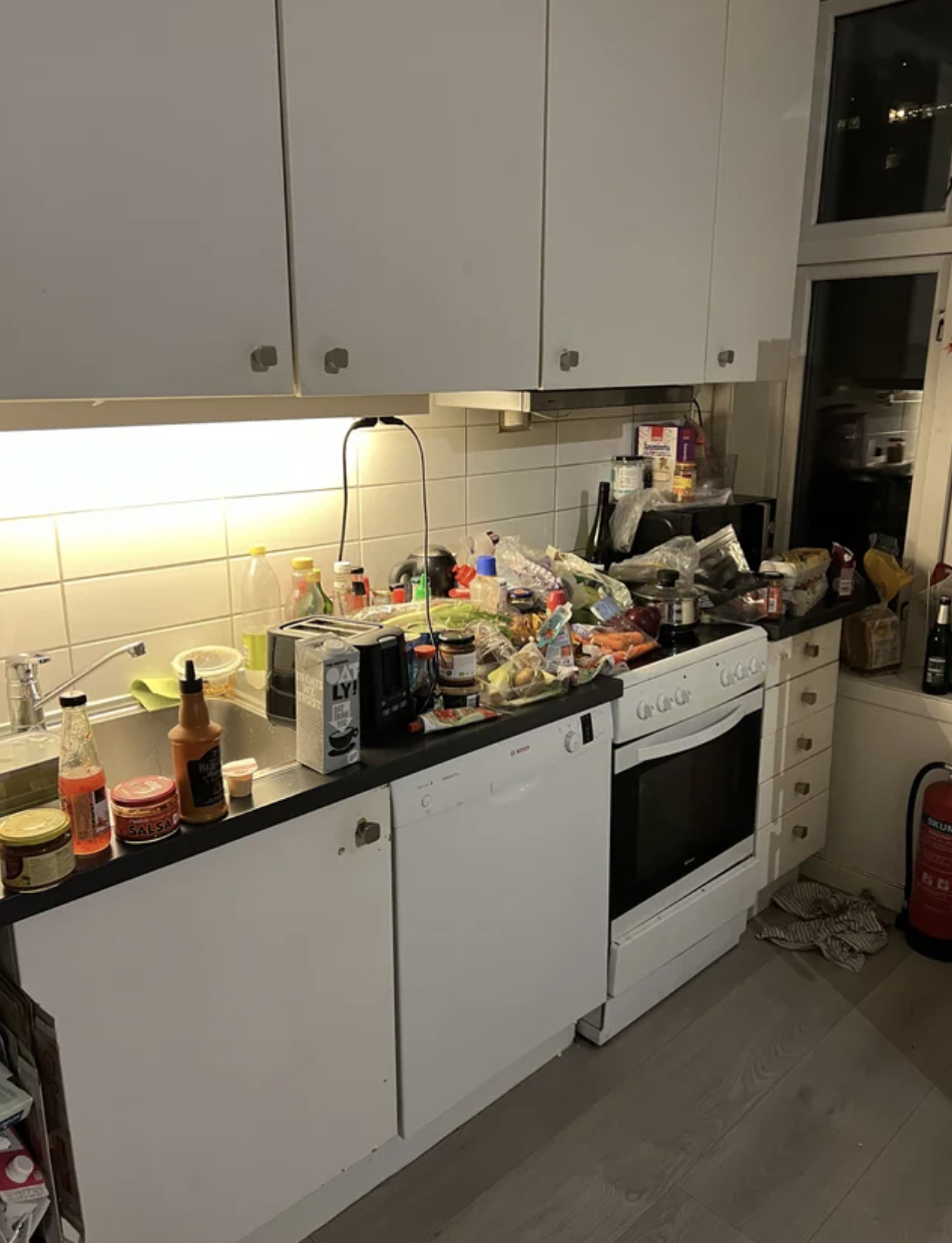 Cluttered kitchen counter with various food items and a stove, reflecting a busy household or cooking session