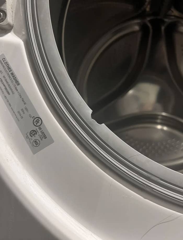 A close-up of a washing machine&#x27;s open door, focusing on a torn rubber seal