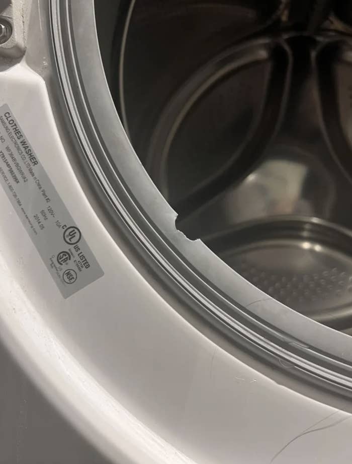 A close-up of a washing machine's open door, focusing on a torn rubber seal