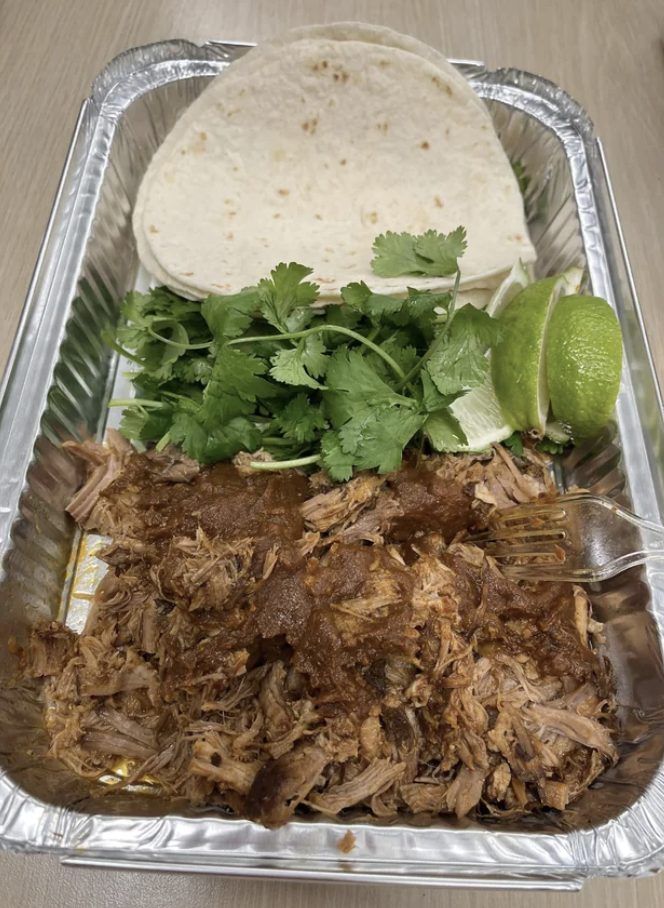 Carnitas with tortillas, lime, and cilantro in a takeout container