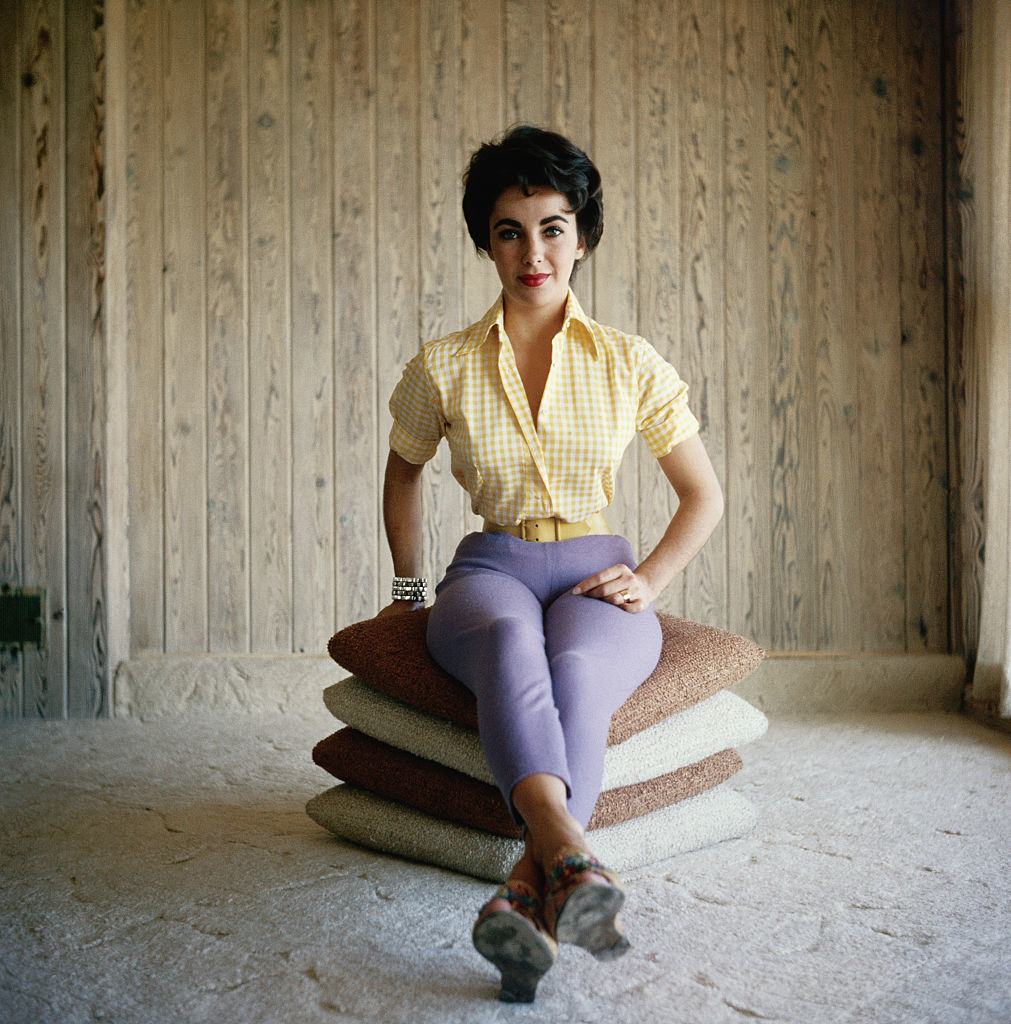 Woman seated on stacked cushions wearing a checkered blouse and lavender pants