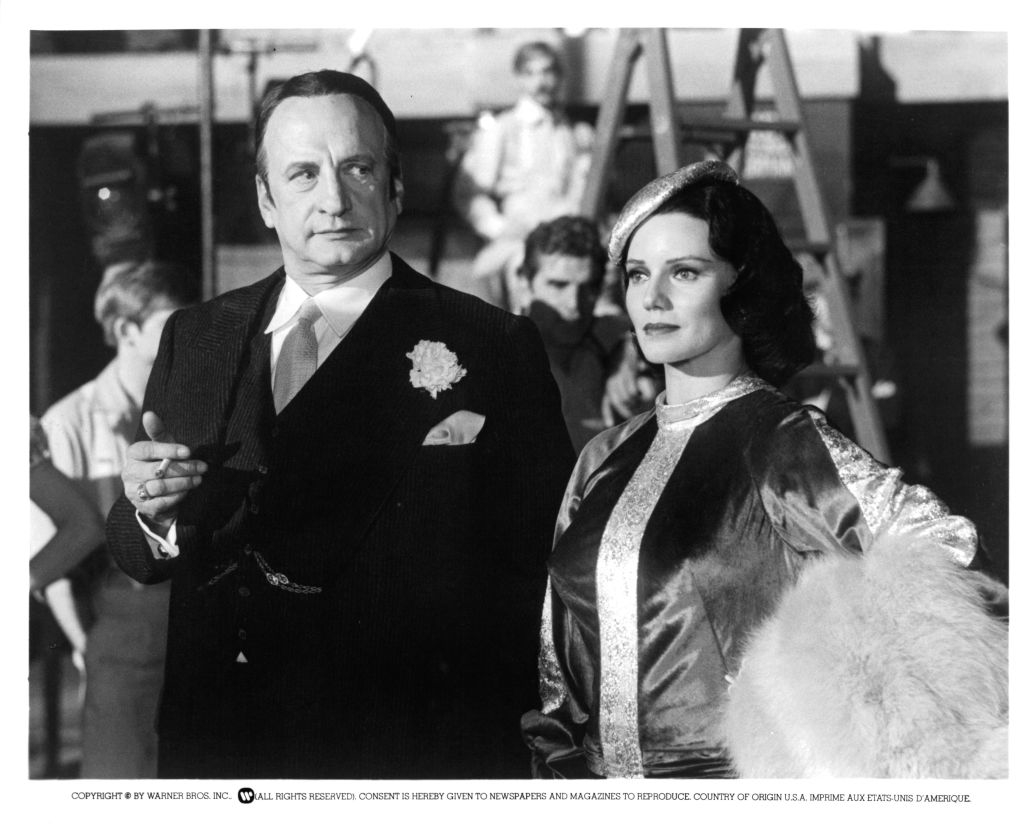 Man in a suit with a flower on lapel and woman in a fur-trimmed cloak stand together in a vintage photo
