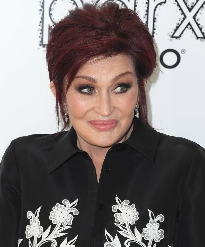 Sharon Osbourne in a black shirt with white floral embroidery, smiling at an event