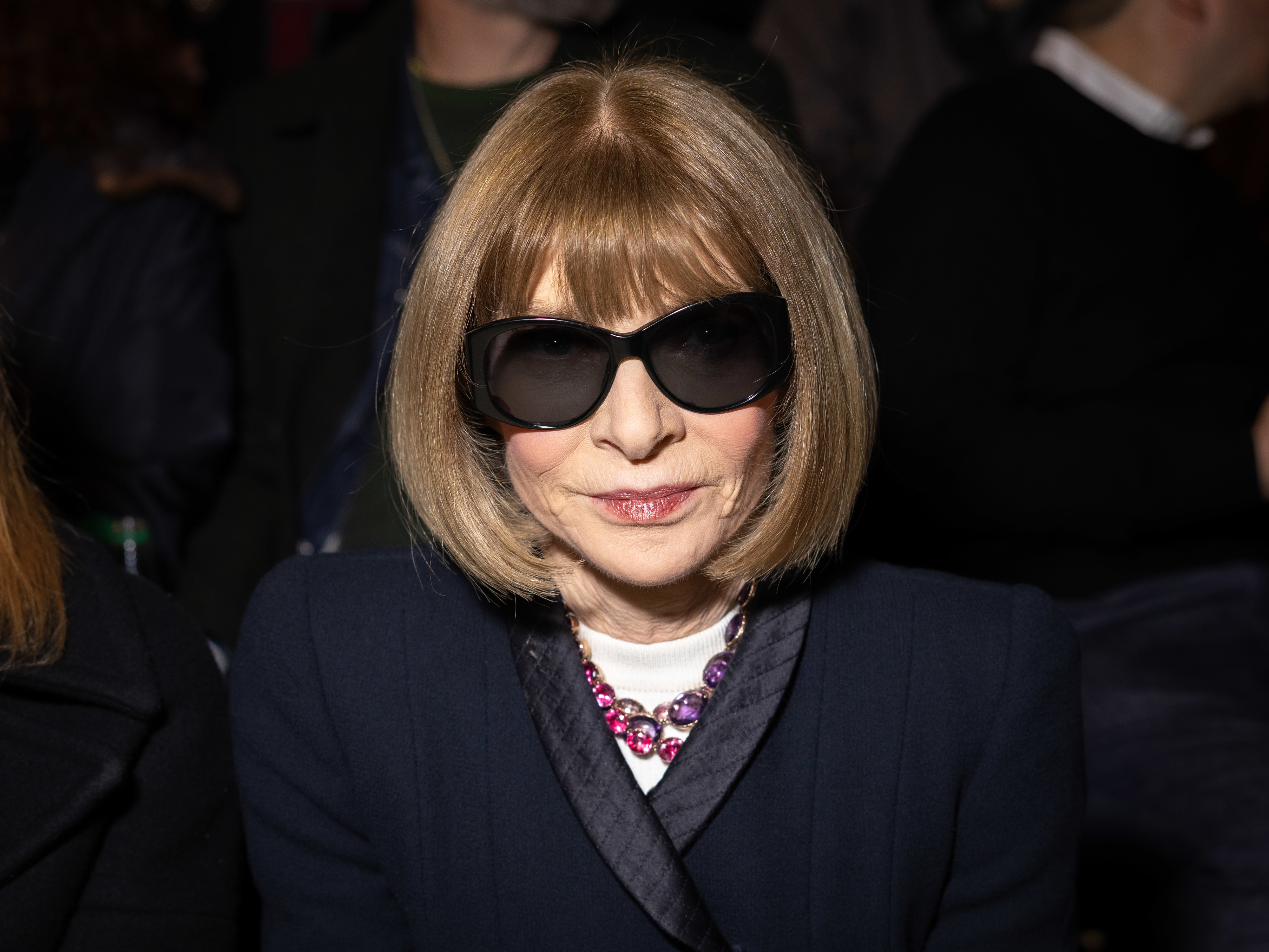 Anna Wintour in a dark jacket, statement necklace, rocking her signature bob hairstyle and sunglasses