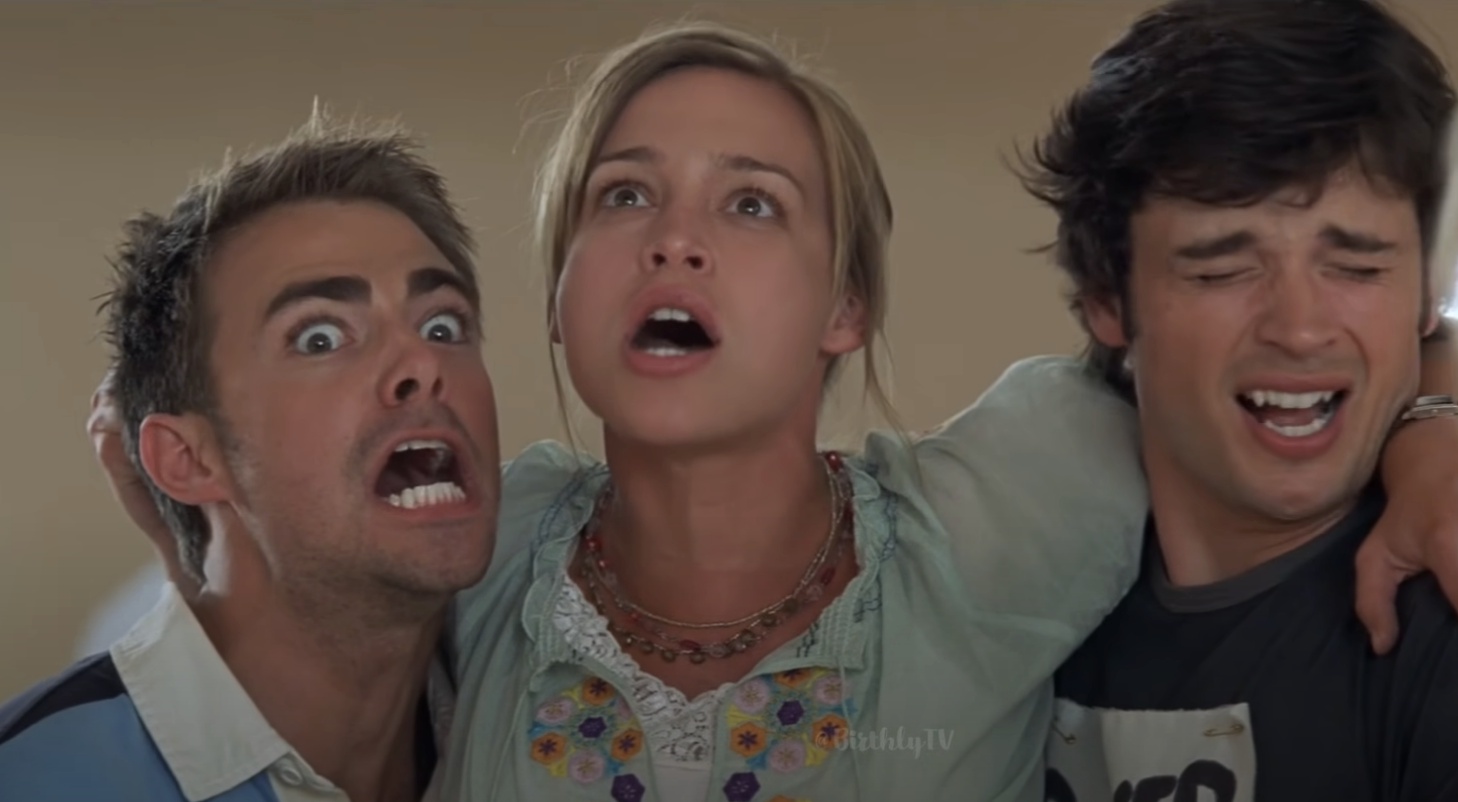 Three characters from a movie appear shocked; man on left makes a funny face, woman in center with necklace, man on right grimaces
