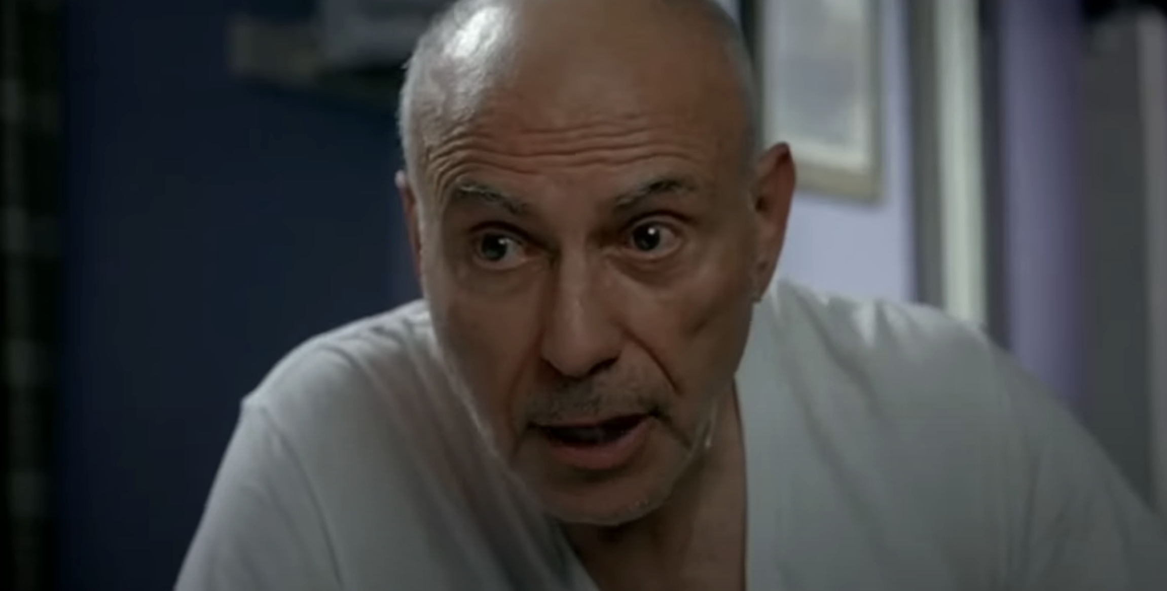 Man with a surprised expression, bald head, wearing a plain T-shirt, indoors