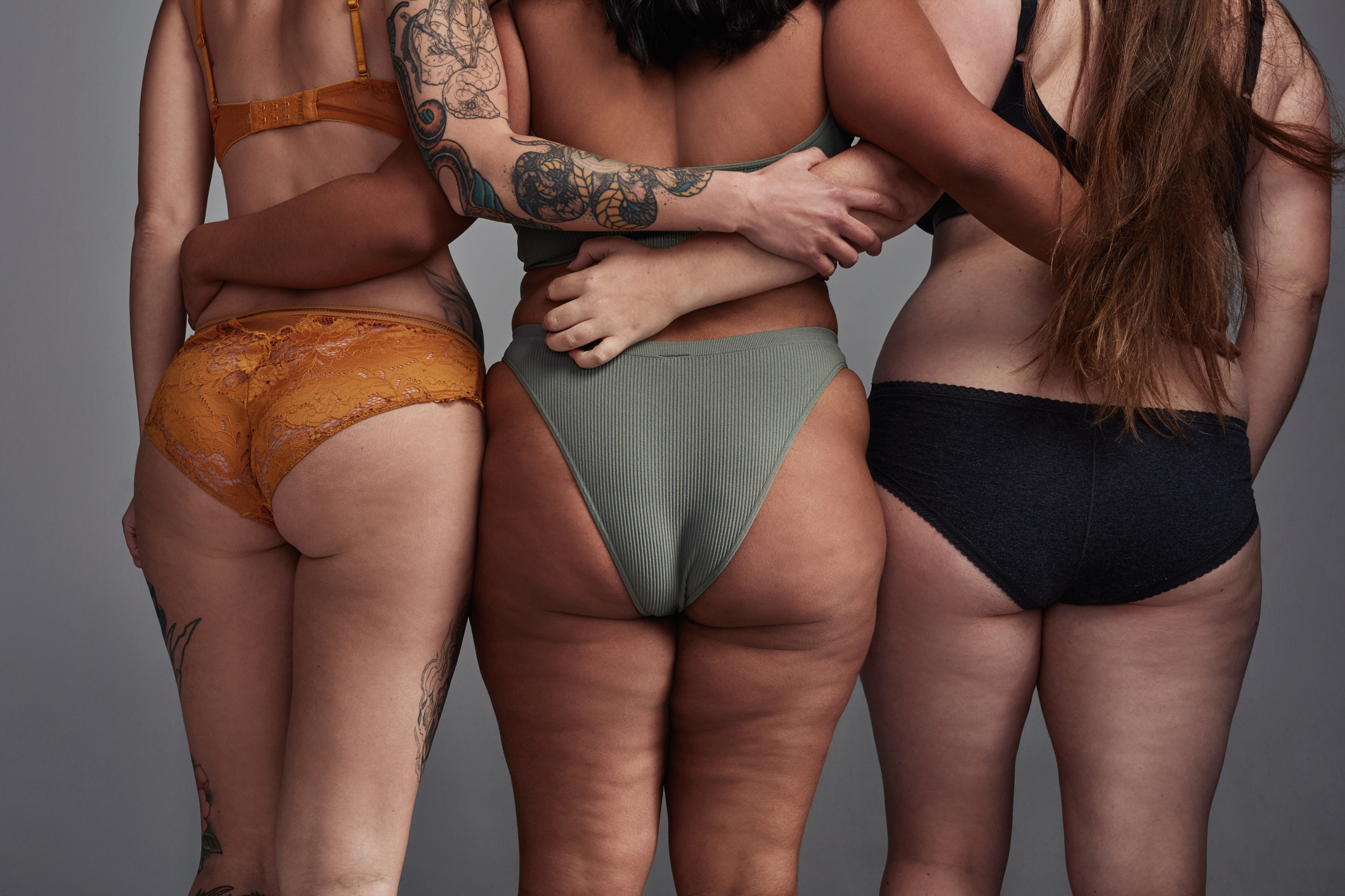 Three individuals standing close, showcasing diverse body types in undergarments, with a focus on body positivity and inclusivity