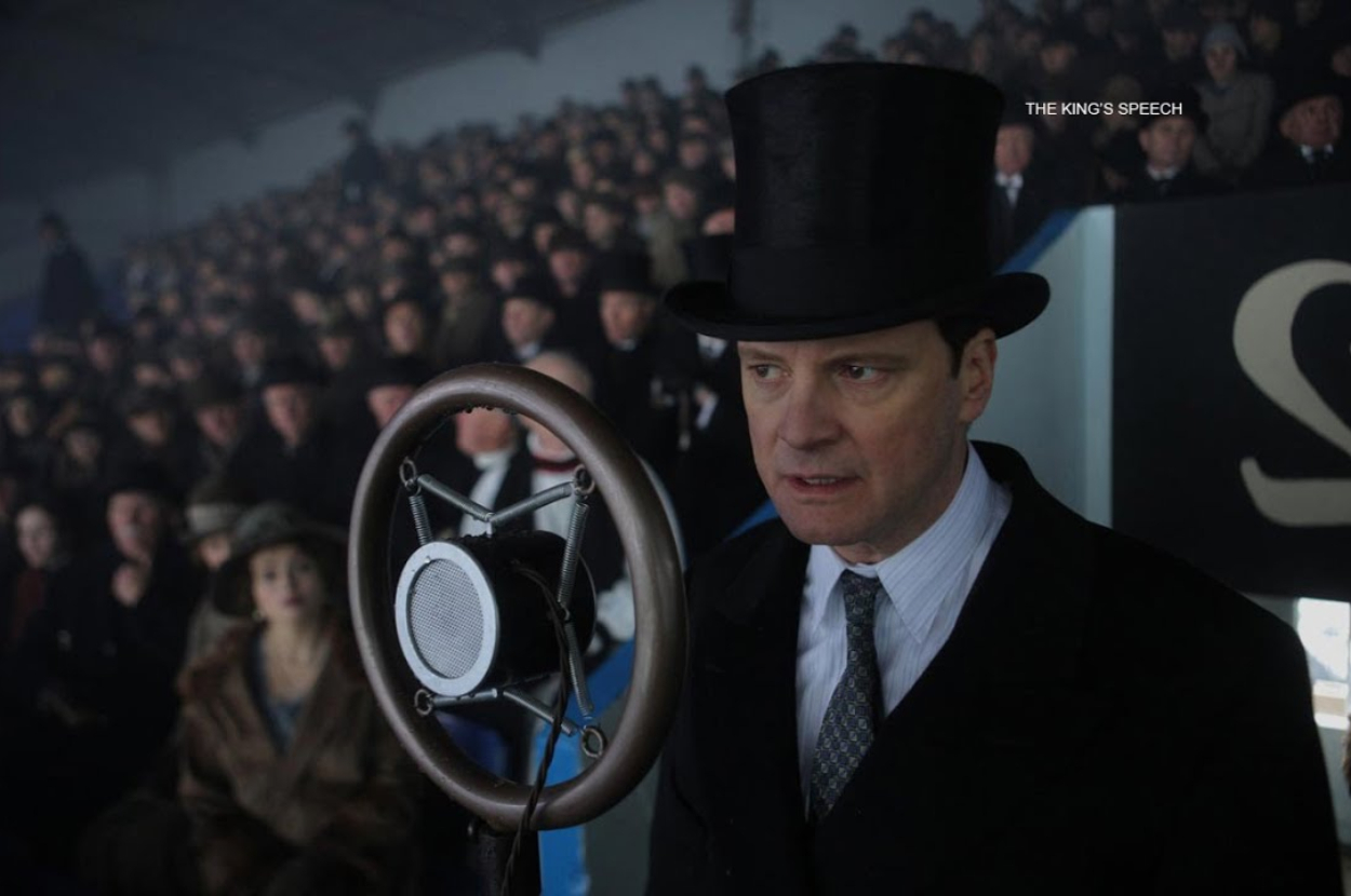 Man in vintage suit and top hat speaks into microphone before crowd, movie scene from &quot;The King&#x27;s Speech&quot;