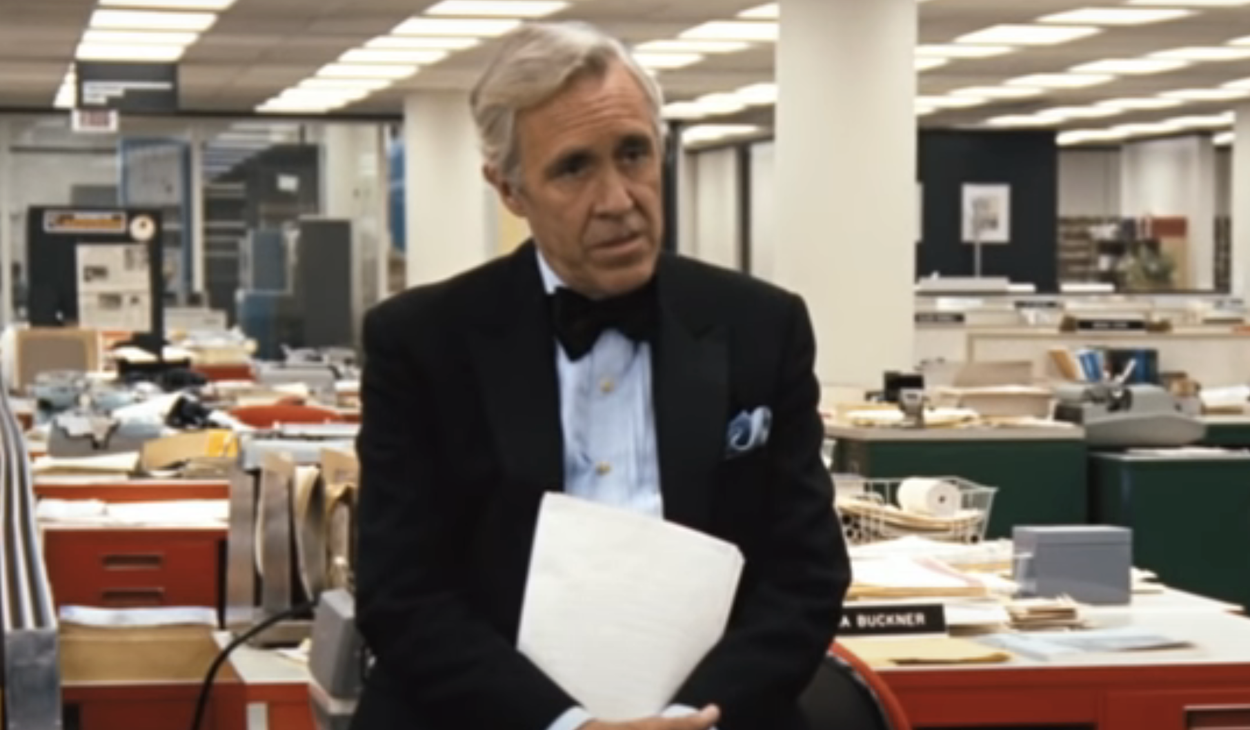Jason Robards sitting on a desk in the newsroom