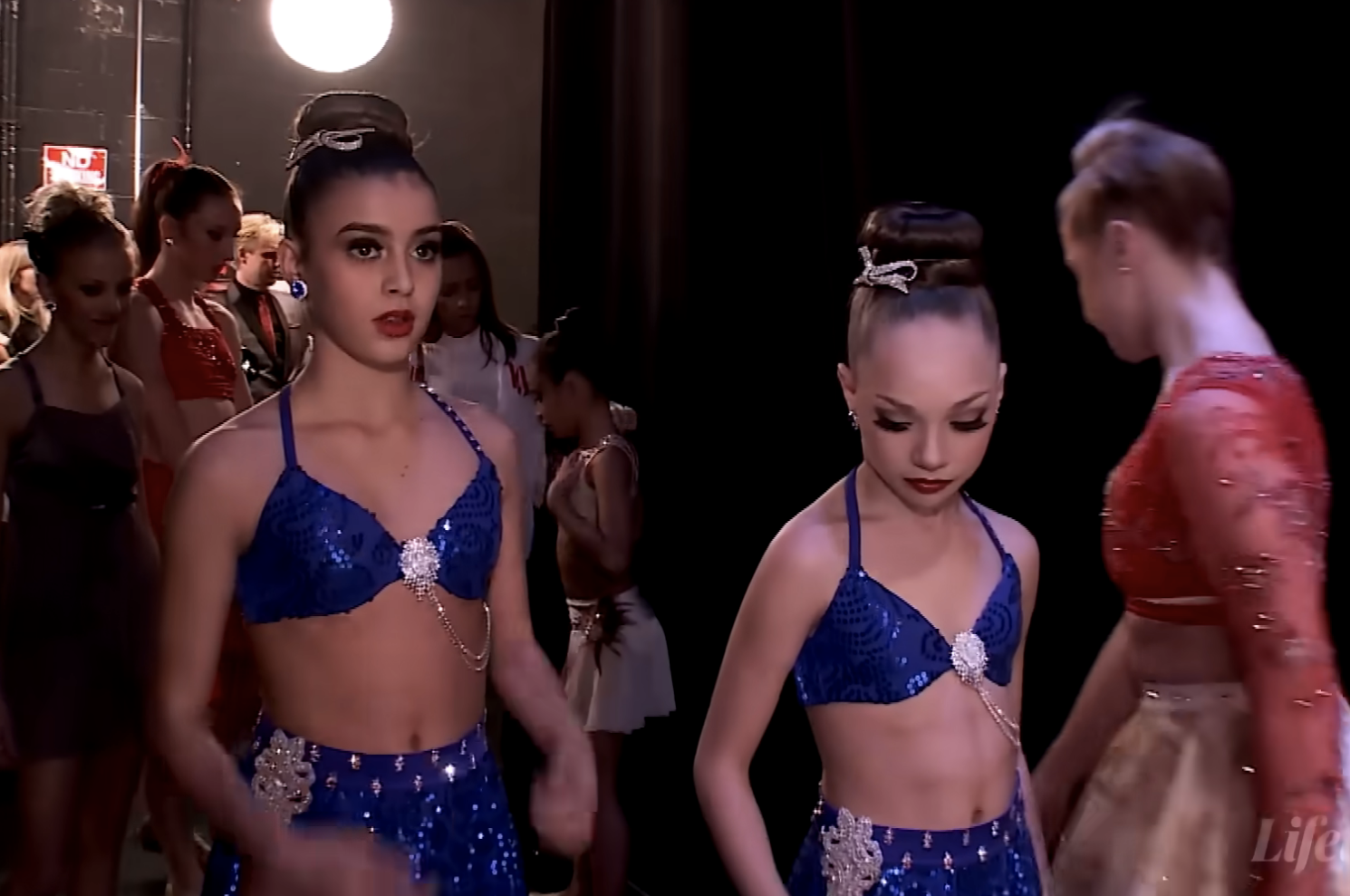 Dance Moms dancers on stage in performance attire with spotlights behind them; YouTube play bar visible