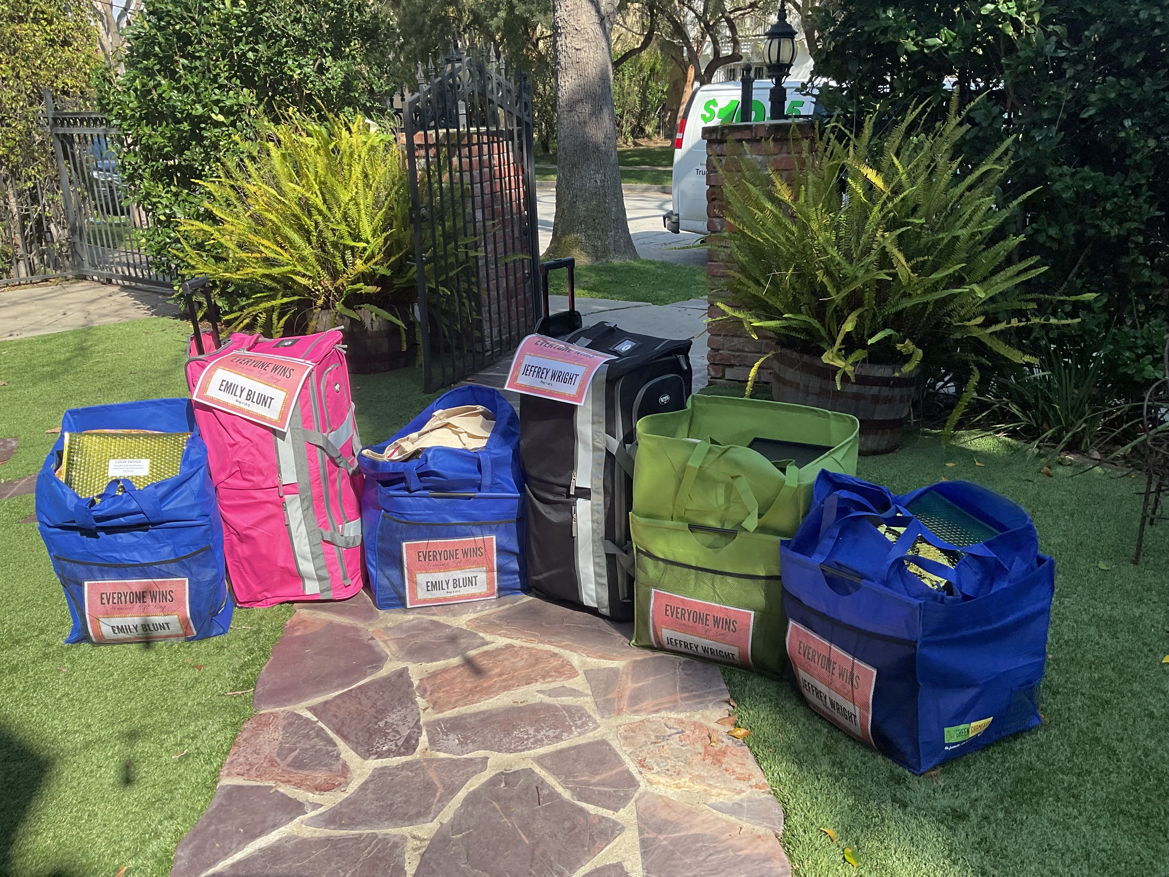 Luggage and bags labeled &quot;Everyone Wins&quot; with celebrity names on them on the grass