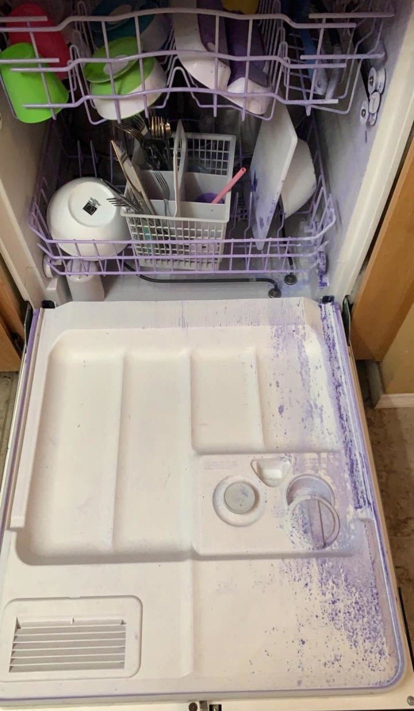 Open dishwasher with dishes and visible detergent spill on door interior