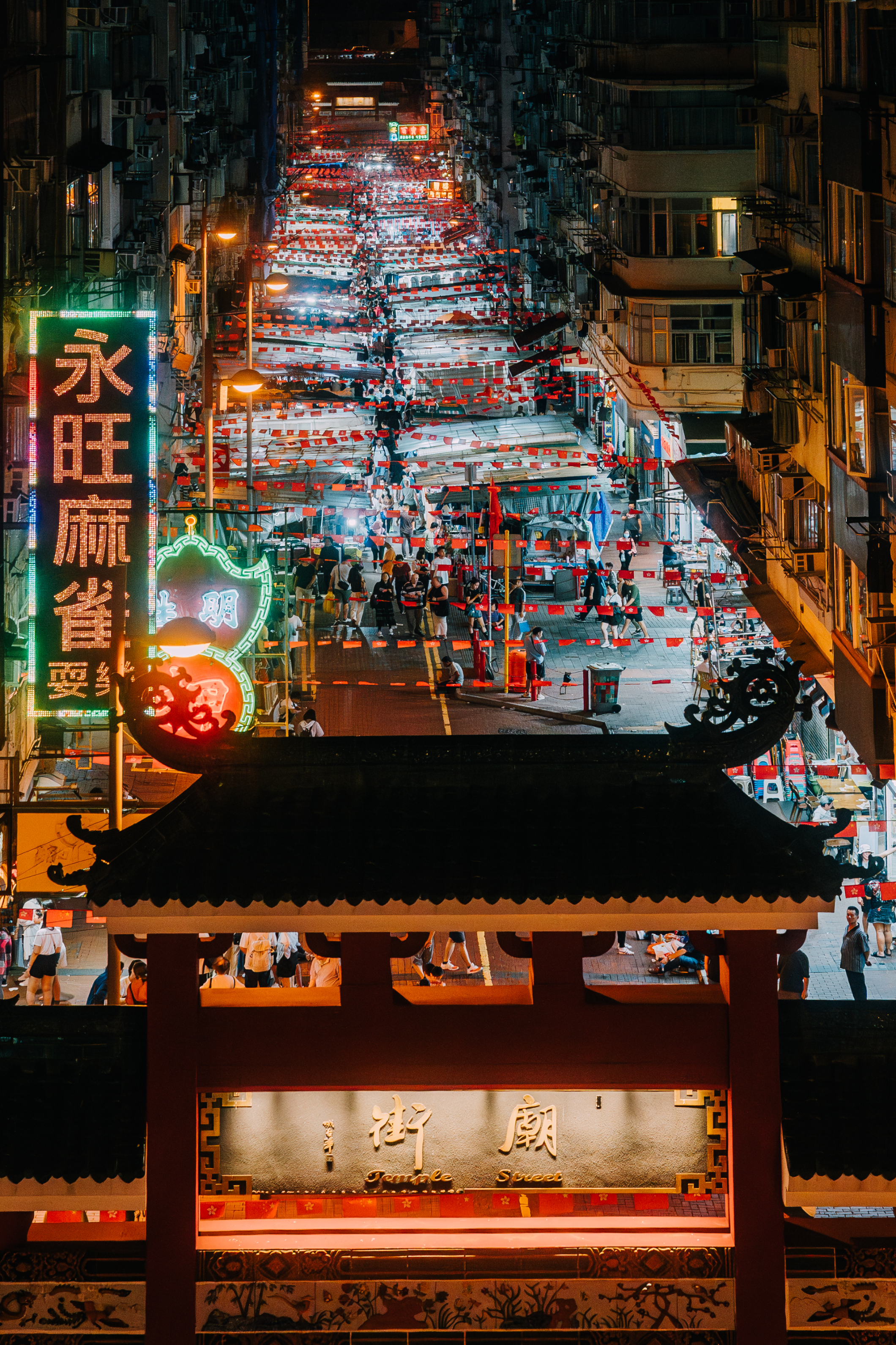 Night view of a busy street market lined with illuminated signs, seen from an elevated perspective