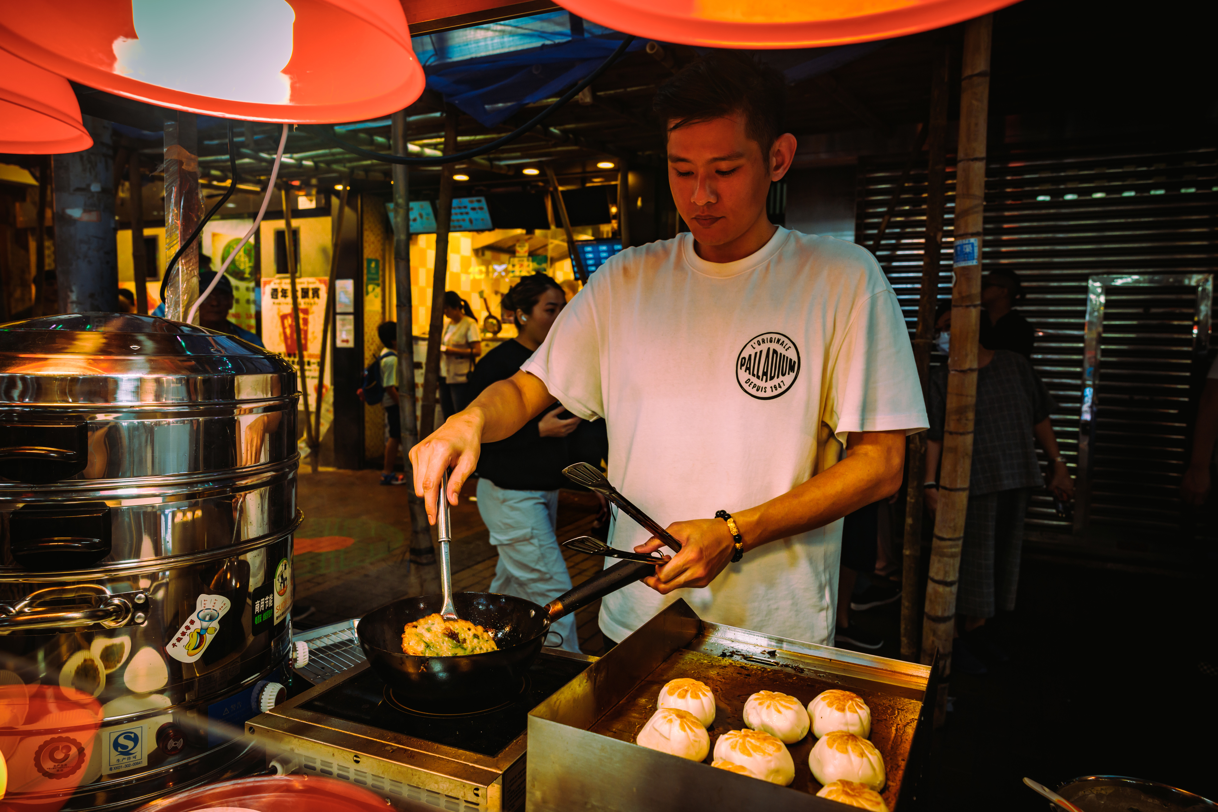 People enjoying street food at a bustling market stall with a vendor cooking