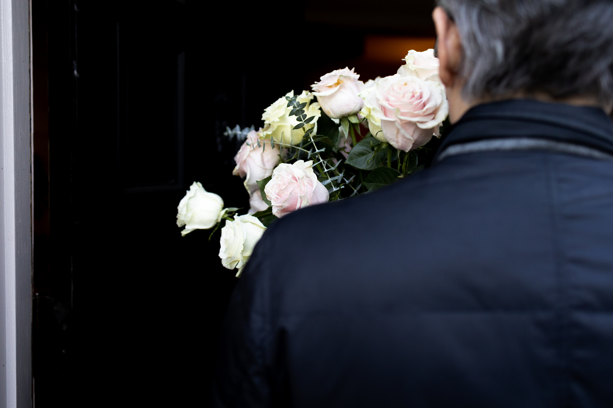 Person holding a bouquet of roses at a doorstep, implying a romantic gesture