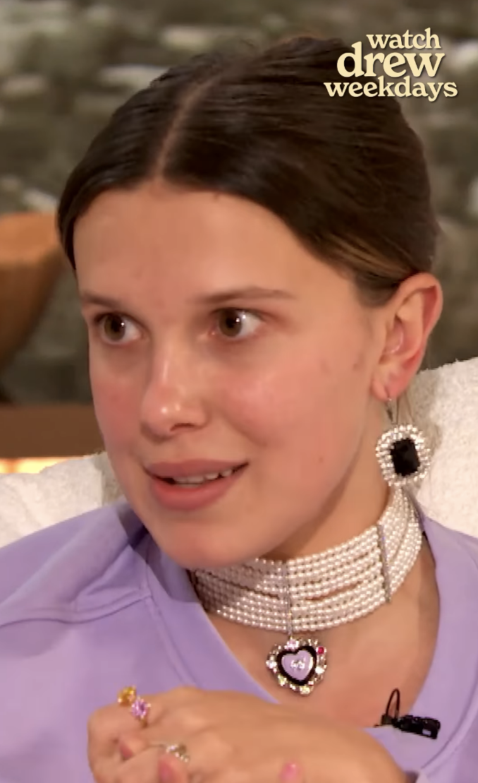 Milie in purple top with embellished choker and large earrings, appearing on the show