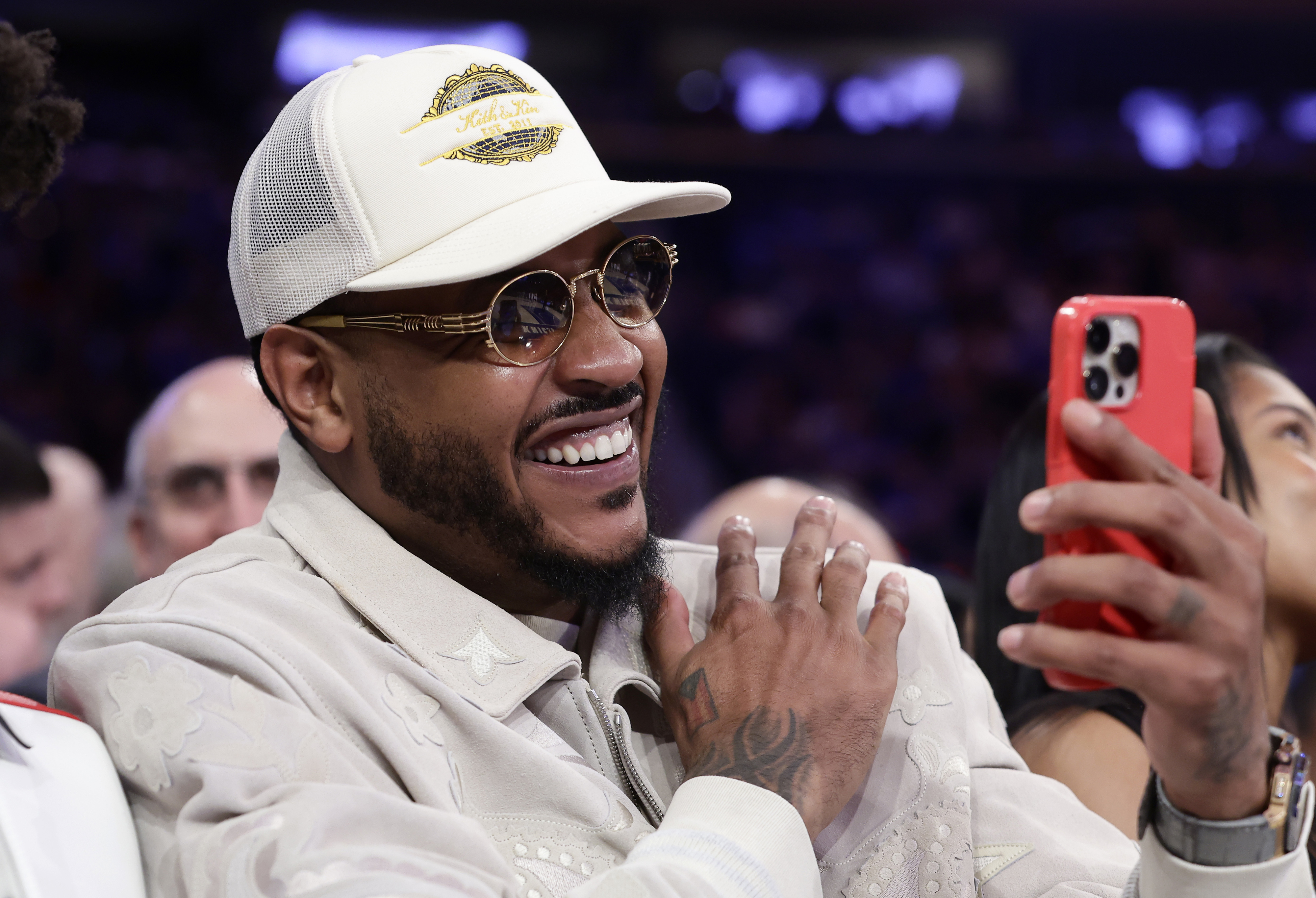 Person smiling and taking a selfie, wearing a cap and sunglasses, casually dressed