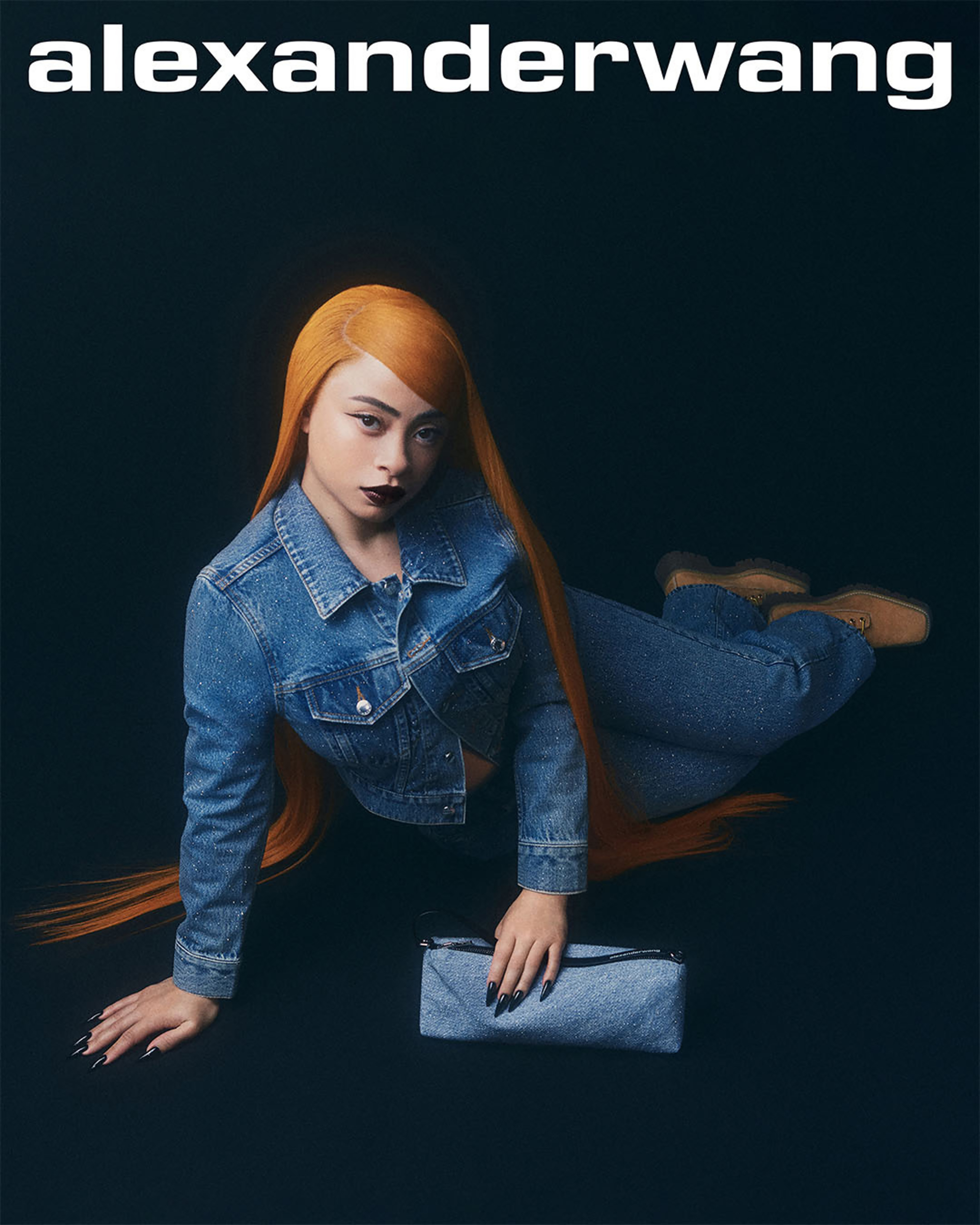 Woman in a denim jacket and pants with a clutch, lying down with flowing hair