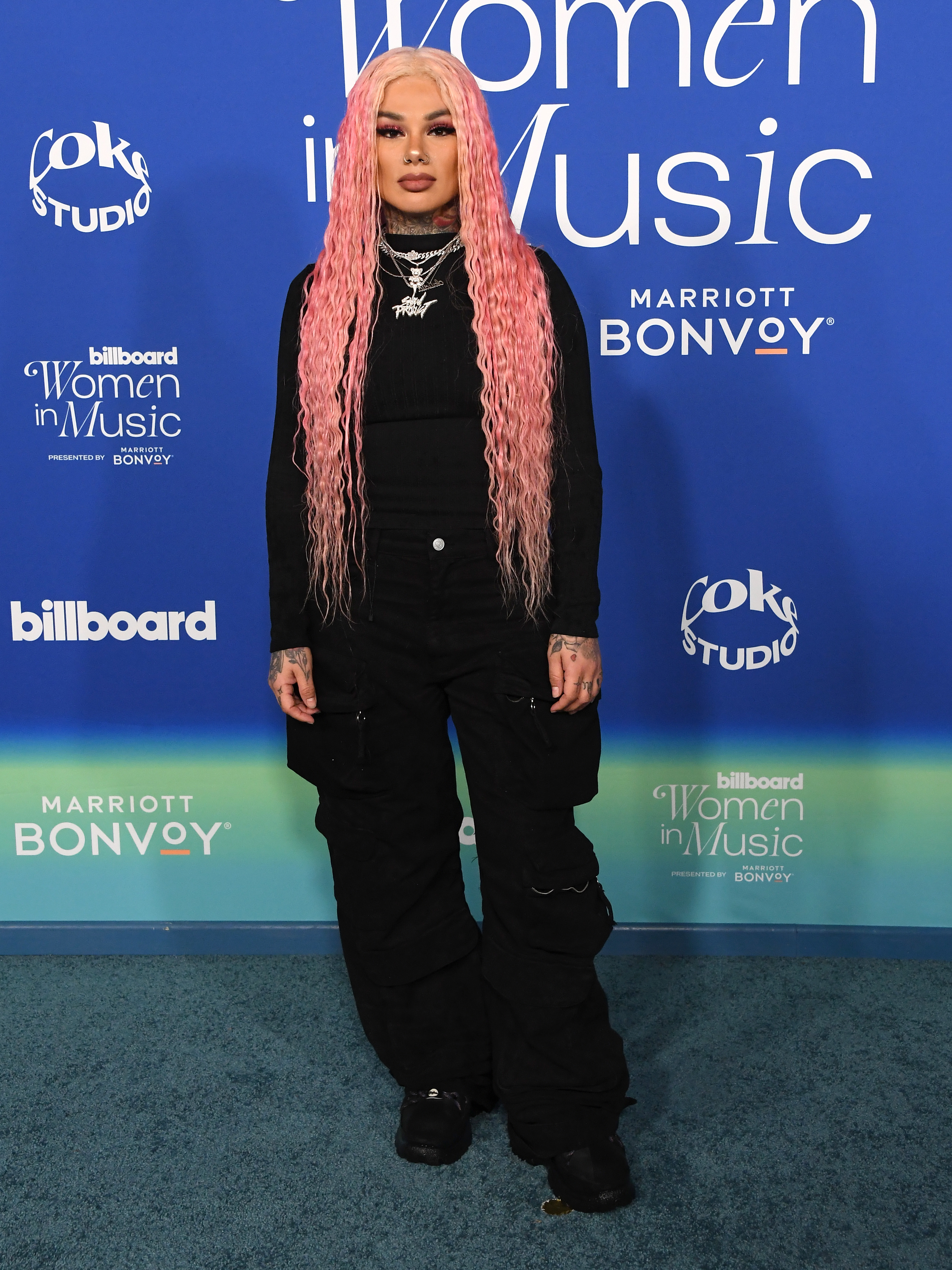 she&#x27;s posing in baggy cargo pants and long sleeved shirt with long pink hair  and silver jewelry