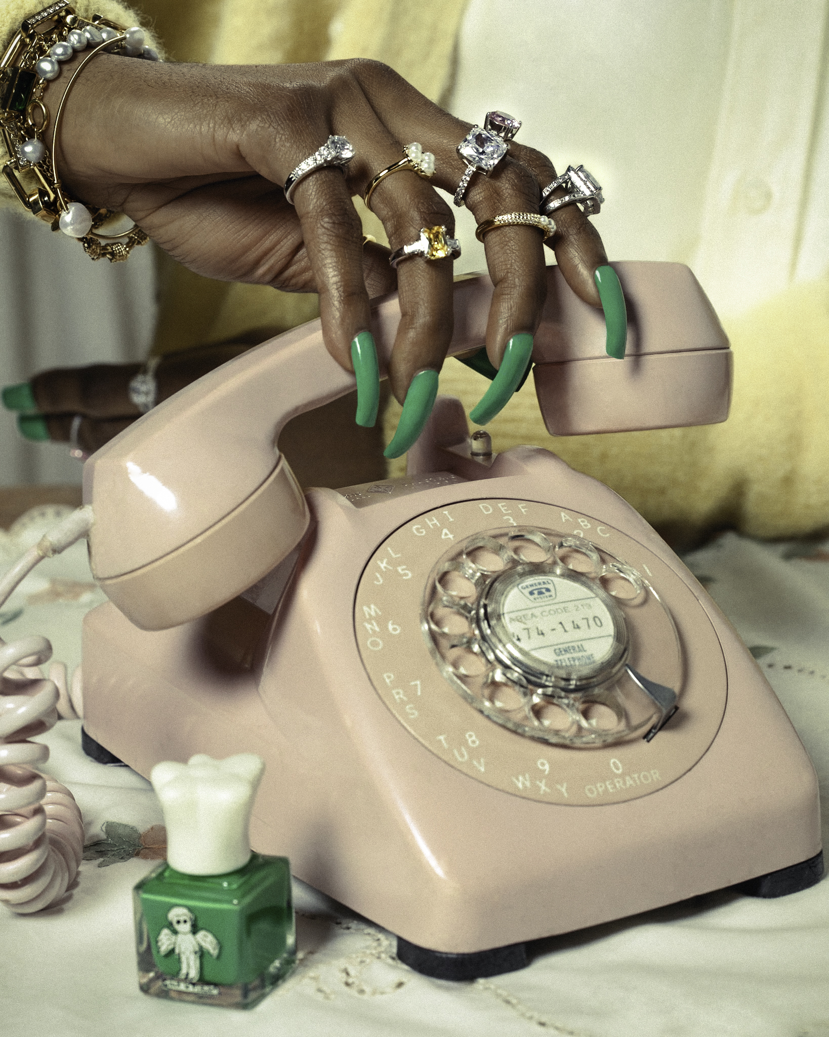 Person&#x27;s hand adorned with multiple rings, holding a vintage telephone receiver, next to a nail polish bottle