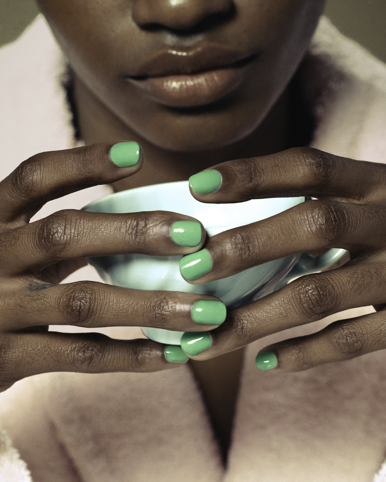 Close-up of hands with vibrant green nail polish cradling a light blue sphere, stylized beauty shot