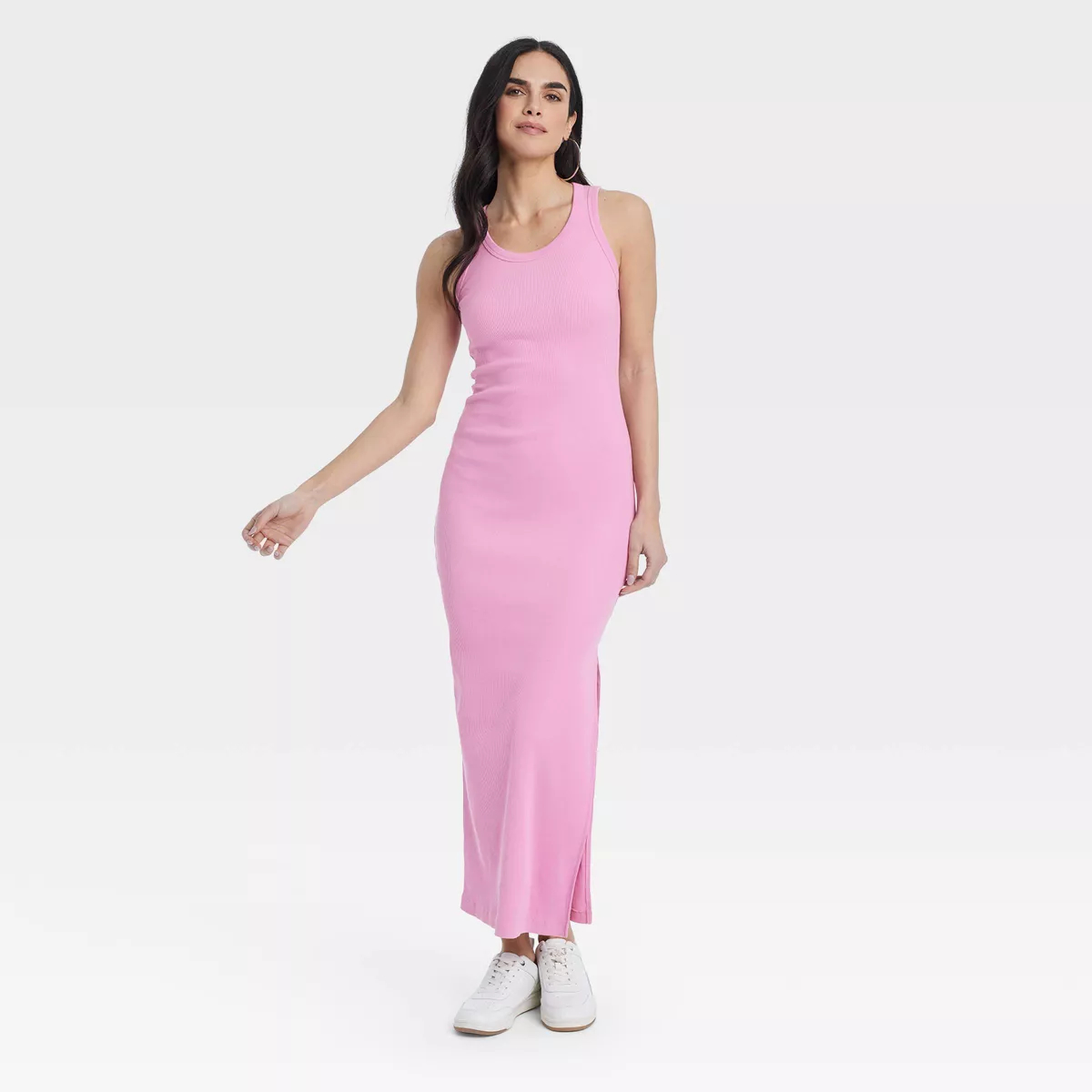 Model in a sleeveless pink dress standing with one hand stretched out, paired with white sneakers