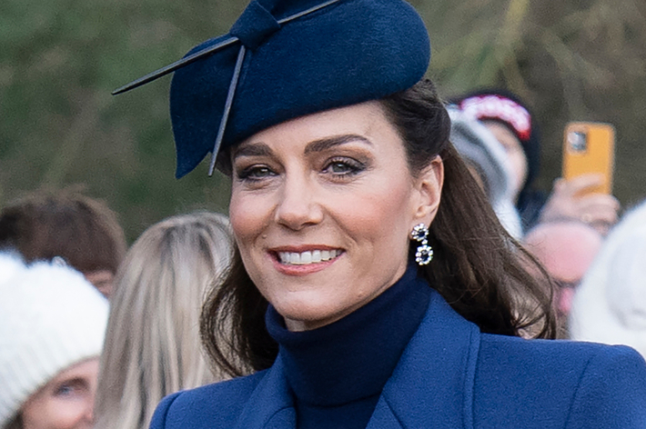 Elegant woman in a fascinator and navy coat at a public event, smiling